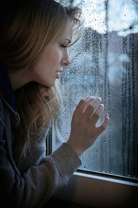 年青的年轻女子透过窗户仰望着雨滴图片