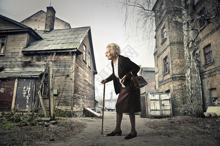 祖母拄着拐杖走在村庄旁背景图片