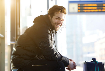 一个快乐的年轻人坐在火车站拿着袋图片