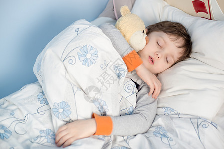 小男孩睡在他的床上抱着一只泰迪熊图片