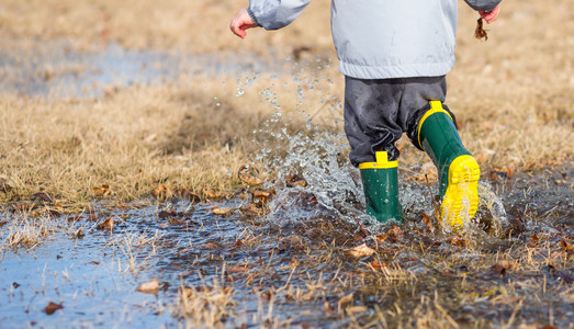 蹒跚学步的孩子穿着雨靴在水坑里奔跑图片