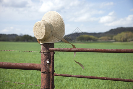 在德克萨斯山乡的一个栅栏柱上坐着一个旧式的稻草帽上面有吹图片