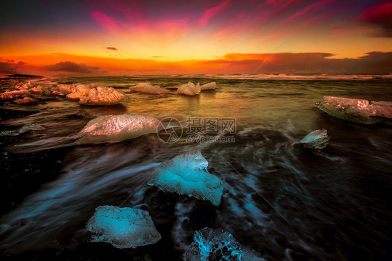 慢速快门照片显示日落期间在冰岛黑沙滩上被冲上岸的冰块周图片
