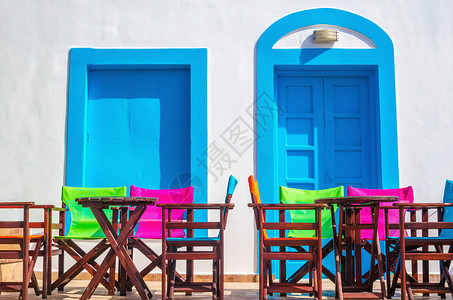 希腊标志蓝木门和白色墙前的多彩希腊餐桌椅和图片
