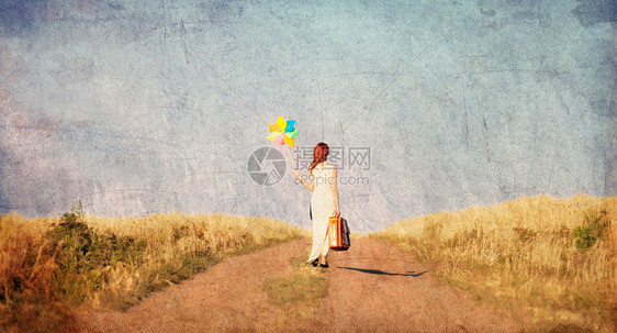 红发女孩在小麦田附近的农村公路上携带手提箱和风玩具图片