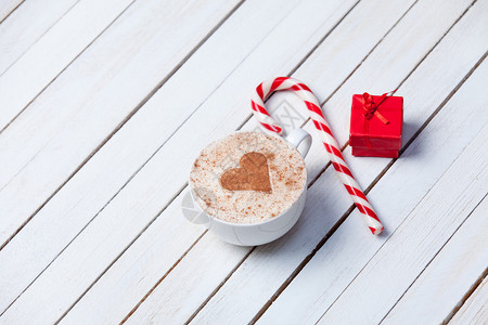 一杯有心脏形状的咖啡和圣诞糖果在白色木头背景的图片