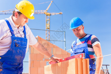 带头盔的建筑工地人或瓦工控制有气泡水平的墙壁或建筑物或在建筑物上图片