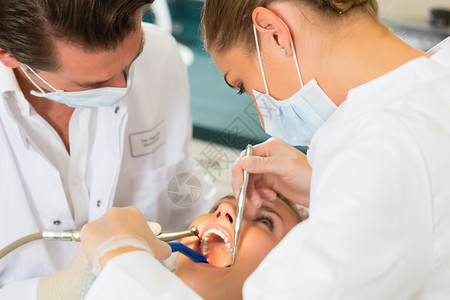 接受牙科治疗戴面罩和手套的牙医和助理女病人图片