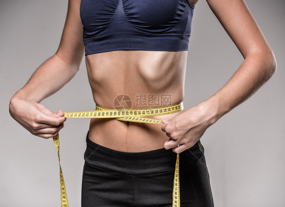 年轻的瘦女人在节食时正在测量她的腰围图片