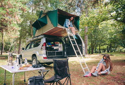 年轻快乐的女士在4x4屋顶的帐篷里休息而其他女人坐在草地上图片