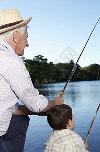 男孩和他祖父带着钓鱼棒在湖底的捕鱼旅图片