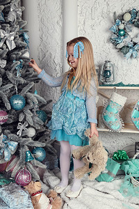 漂亮的小女孩靠近树圣诞树附近穿着蓝色连衣裙的漂亮女孩带着图片