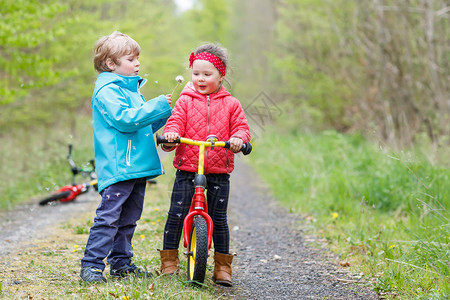 两个穿着鲜艳夹克的可爱微笑孩子在雨天骑着自行车在森林里散步兄弟姐妹之间的友谊幸图片