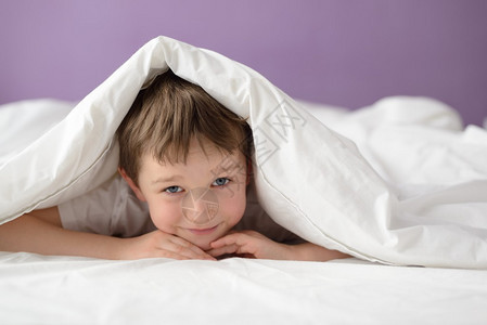快乐的男孩躲在白色毯子或床罩下的床上男孩在床上图片