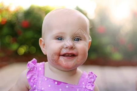 一个超级快乐的10个月长着新前牙的女婴在夏天坐在花图片