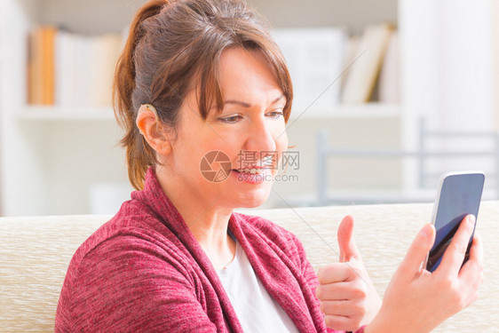 微笑的聋哑妇女使用手语在智能手机的图片