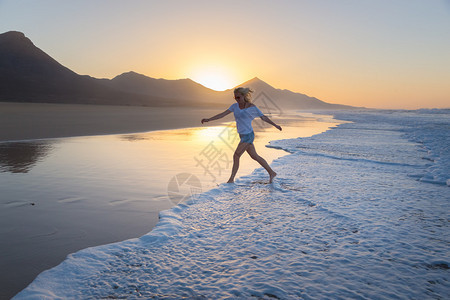 女人在日落时分在孤独的沙滩上从海浪中奔跑海浪扫去她在沙滩上的痕迹海滩图片