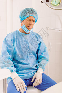 身穿外科手术服的疲劳的外科医生坐在图片