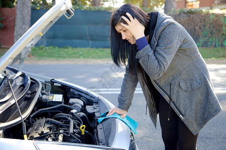 不快乐的女人看着坏掉的汽车引擎图片