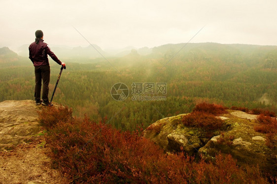 深色运动服和极杆上的人登山者站在山峰岩上图片