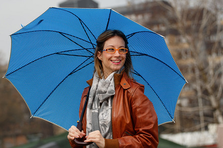 下雨天带着蓝伞的快乐年轻女人背景图片