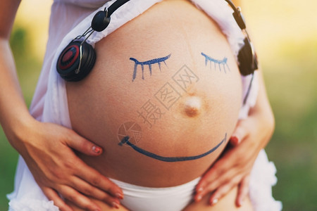 孕妇腹部特写与笑脸画在户外听音乐在女人肚子上的耳机怀孕快乐图片