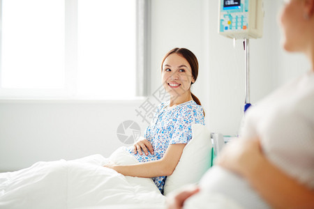 坐在床上与一名病人交谈的年轻怀孕背景图片