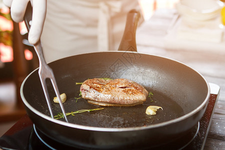 平底锅上的肉和香草手拿着肉叉加入一些大蒜和香草图片