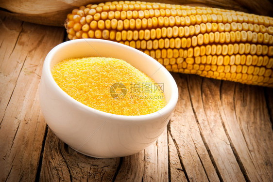 木制背景上的干玉米种子碗里的玉米粉图片