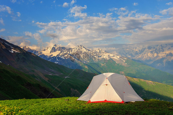 高草地上的灰色帐篷在山脉和岩石背图片