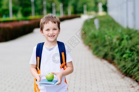 7岁小男孩在上学路上带着书和苹果穿着白图片
