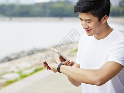 亚洲年轻男子使用智能手机和智能手表中的应用程序在锻炼期间图片