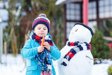 可爱的蹒跚学步的男孩堆雪人图片