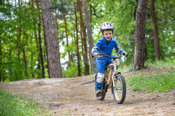 穿着五颜六色的雨衣的快乐有趣的小男孩在寒冷的森林里骑着他的第一辆自行车户外儿童的积极休闲快乐无忧图片