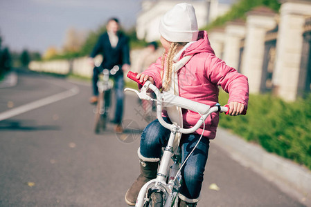 可爱小女孩骑自行车和看着父亲的近视肖像图片