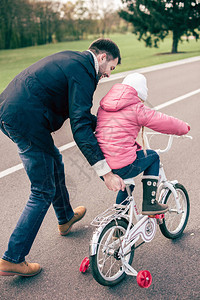 快乐的父亲教他可爱的小女儿在沥青路上骑自图片