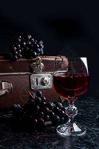 深色大理石背景上的单杯红酒深色大理石背景上的蓝色成熟葡萄黄色篮子里的成熟葡萄和背图片