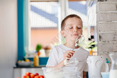 儿童从搅拌器搅拌器中品尝糕点男孩在厨房帮忙和图片