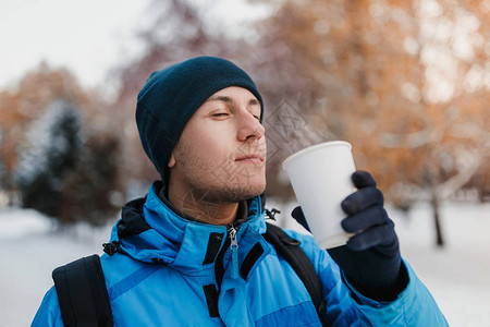 在冬季公园户外喝热饮的热饮料穿着温暖帽子和蓝夹克的图片