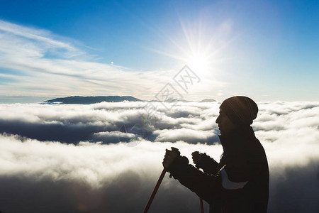 日落时在云层上方高山上的登山者剪影图片
