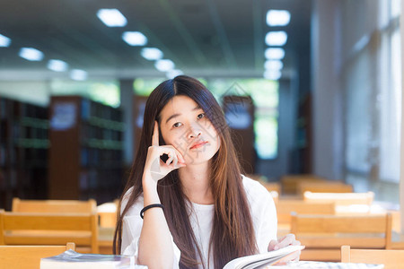 快乐女学生在图书馆阅读书时坐在窗外的木椅子上图片