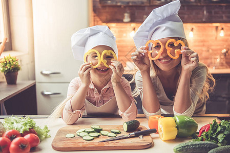可爱的小女孩和她美丽的妈在厨师的帽子她在家厨房做饭图片