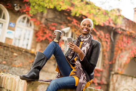Atrractive非洲女在秋季公园使用手机和咖啡图片