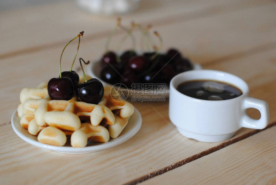 木制桌上的华夫饼樱桃和咖啡白杯图片