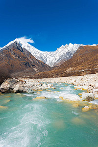 尼泊尔高海拔快速流动的冰川水河后面的白雪皑的喜马拉雅山脉的一部分图片