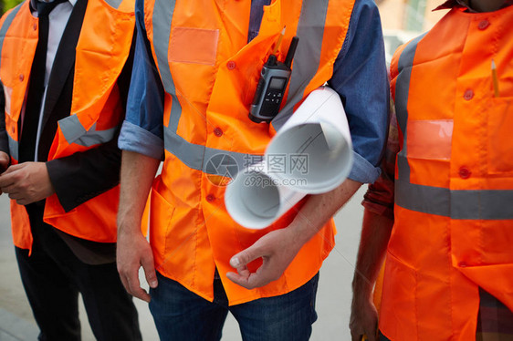 三名身穿橙色反光背心的建筑工人站在工地上拿着建图片