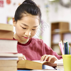 在教室里读一本厚书的亚洲小学生背景图片