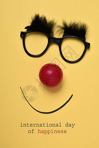 文字国际快乐日和一副眼镜眉毛细布红小丑鼻子和黄色背景的图片