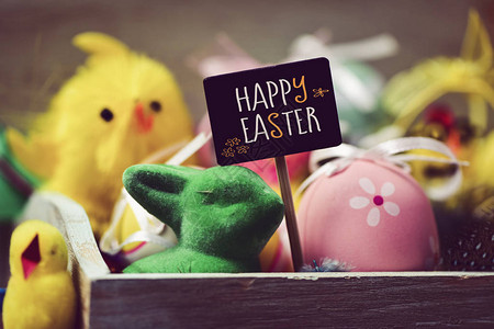 一些黄色玩具小鸡一只绿色玩具兔一些装饰过的鸡蛋和一个黑色招牌图片