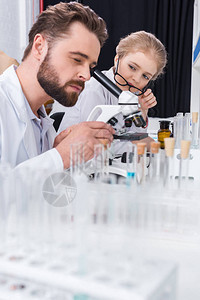 有眼镜的小学生看着在实验室用显微镜工作图片